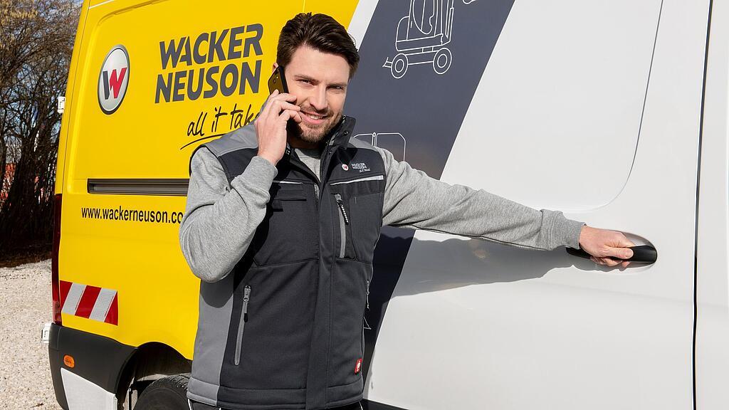 Een medewerker van Wacker Neuson staat voor een Wacker Neuson-servicevoertuig en telefoneert.