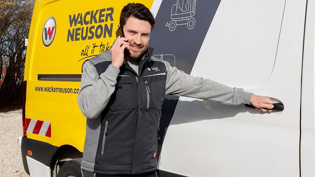 Un collaborateur Wacker Neuson est au téléphone devant un véhicule de service Wacker Neuson.
