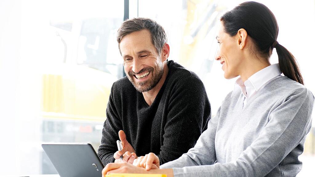 Customer sitting with Wacker Neuson salesperson in front of laptop, being advised on used construction machines and construction equipment.