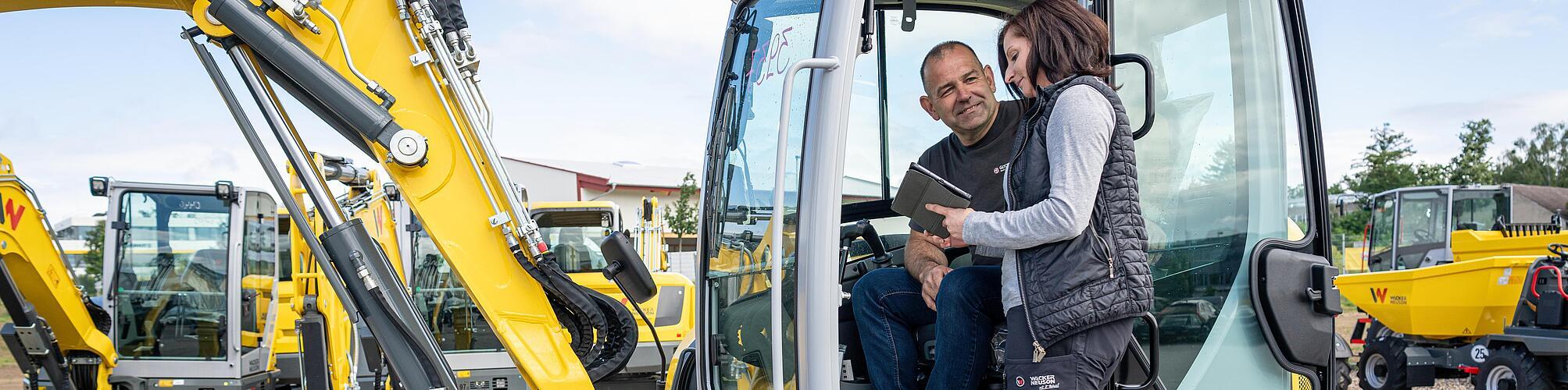 zwei wacker neuson mitarbeiter kontrollieren einen bagger