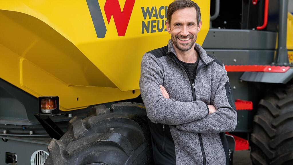 Een klant van Wacker Neuson staat glimlachend met gekruiste armen voor een Wacker Neuson-wieldumper.
