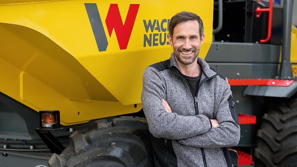Un client Wacker Neuson souriant et les bras croisés devant un dumper sur pneus de Wacker Neuson.
