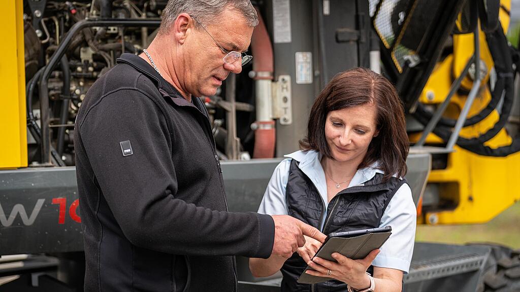 two persons discussing in front of a wacker neuson machine