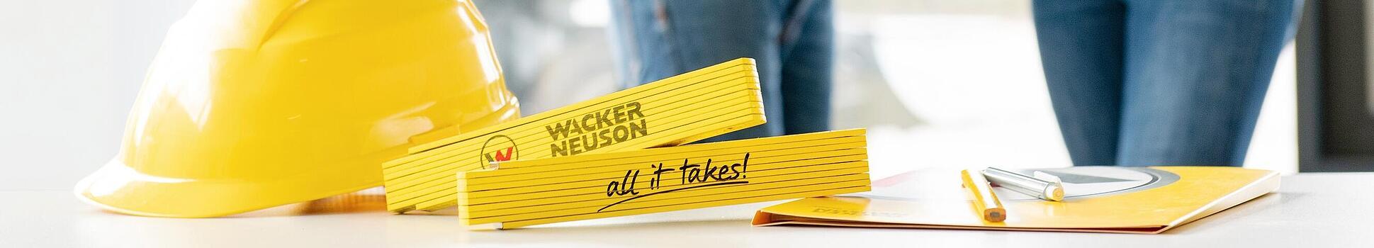 Wacker Neuson merchandise items lying on table in foreground, Wacker Neuson employees in background.