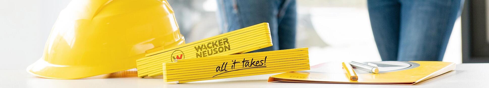 Artigo de merchandising da Wacker Neuson está em uma mesa em primeiro plano, com os funcionários da Wacker Neuson em segundo plano.