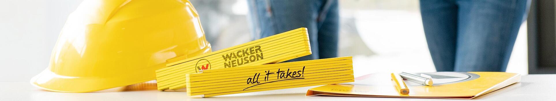 Wacker Neuson merchandise items lying on table in foreground, Wacker Neuson employees in background.