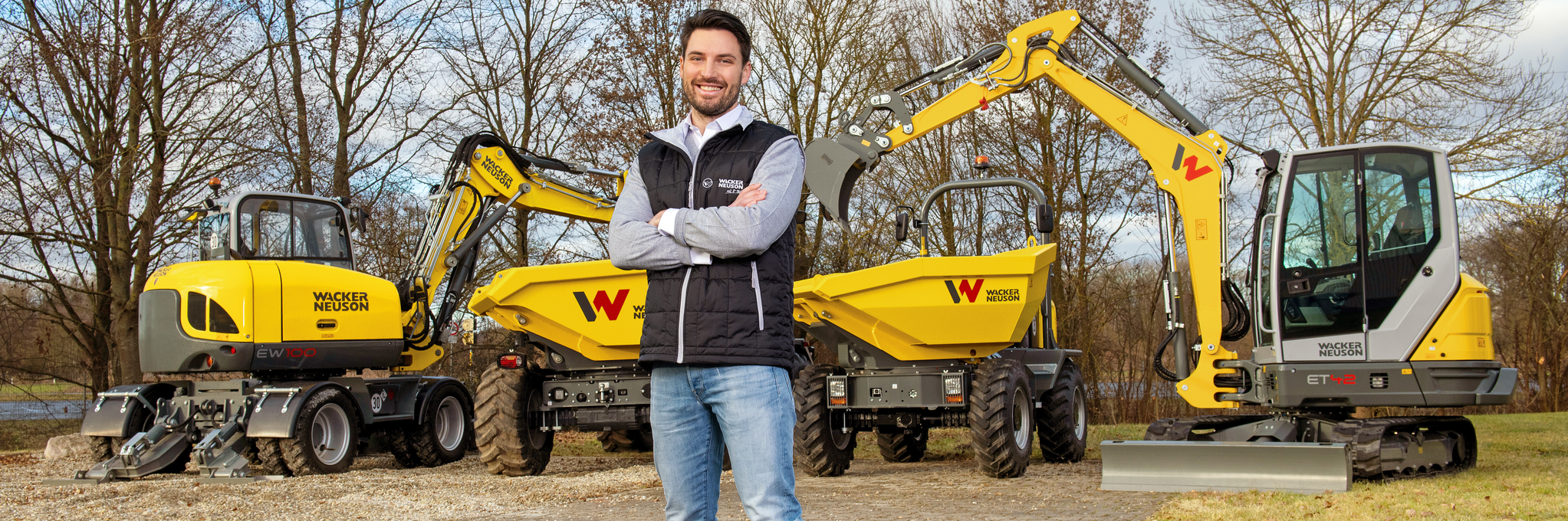 Přátelský zaměstnanec Wacker Neuson stojí před stavebními stroji Wacker Neuson.