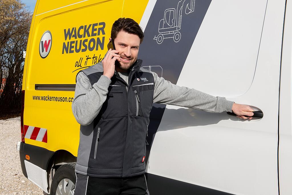 Un collaborateur Wacker Neuson est au téléphone devant un véhicule de service Wacker Neuson.