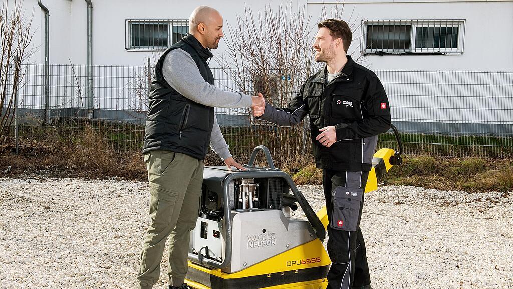 Wacker Neuson employee shaking a customer’s hand in front of a Wacker Neuson vibratory plate.