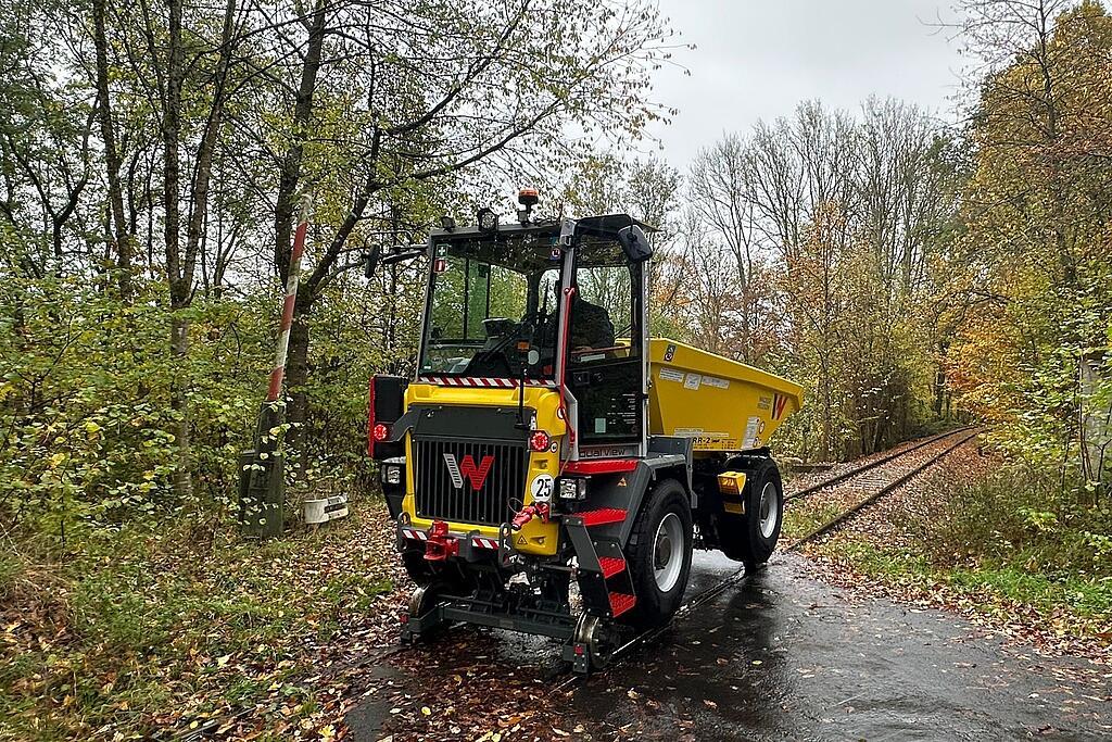 Gelber Zweiwege-Baustellen-Dumper auf Eisenbahnschienen im Herbstwald bei nasser Strecke