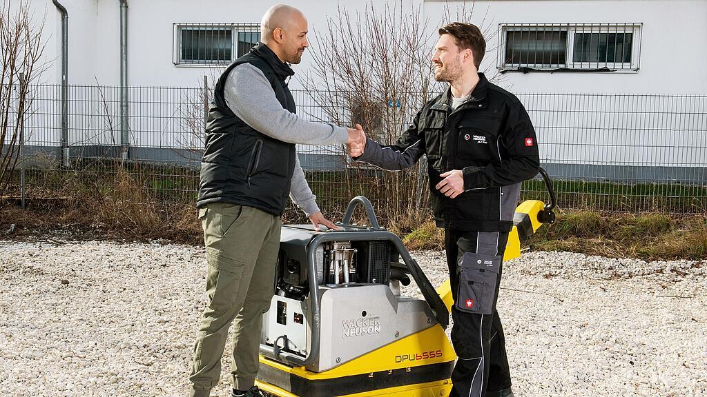 Wacker Neuson employee shaking a customer’s hand in front of a Wacker Neuson vibratory plate.