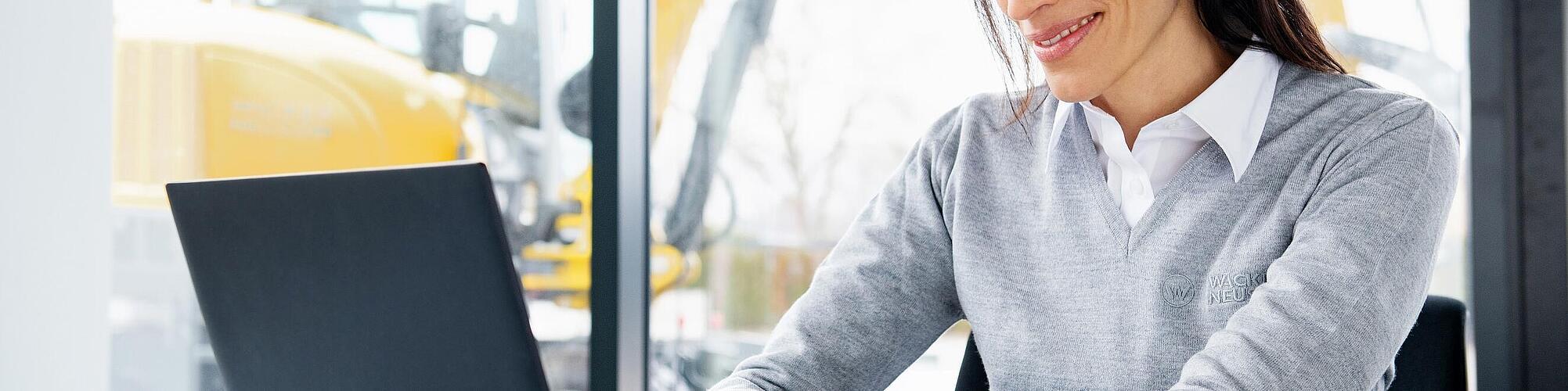 Wacker Neuson employee sitting at a laptop and smiling.