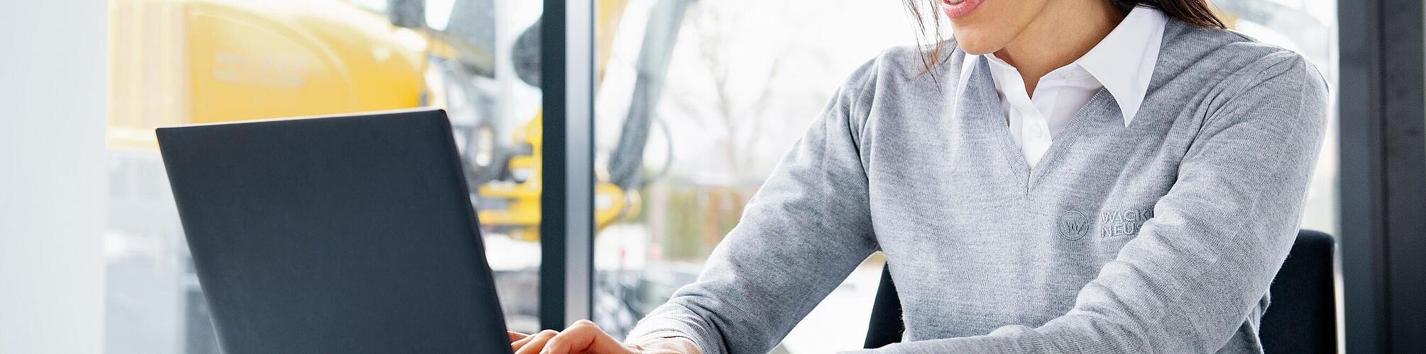 Wacker Neuson employee sitting at a laptop and smiling.