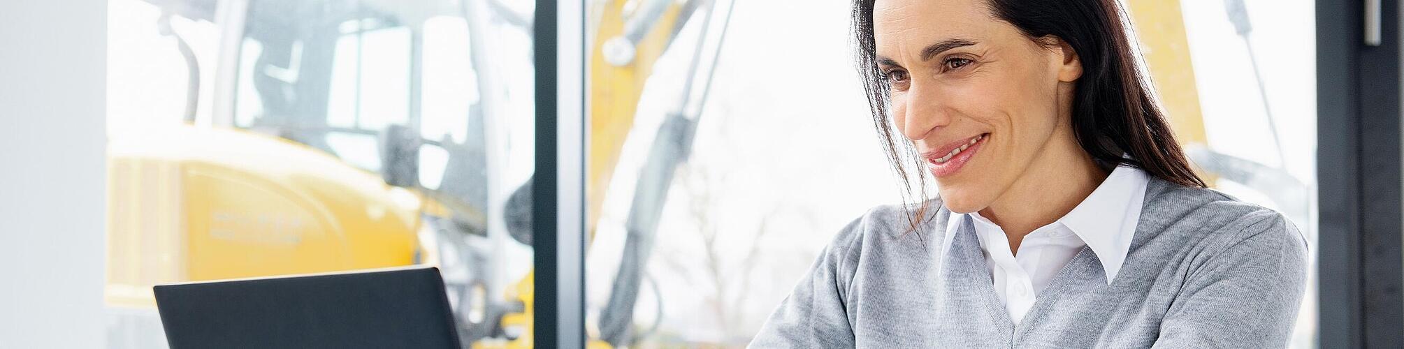 Une collaboratrice Wacker Neuson est assise devant un ordinateur portable et sourit.