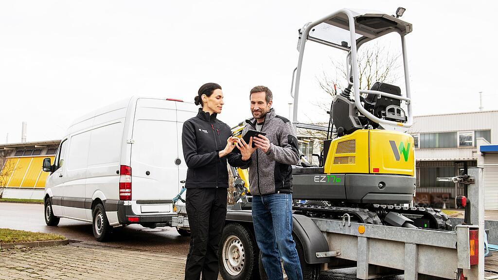 Wacker Neuson-merchandise op tafel op de voorgrond, Wacker Neuson-medewerkers op de achtergrond.
