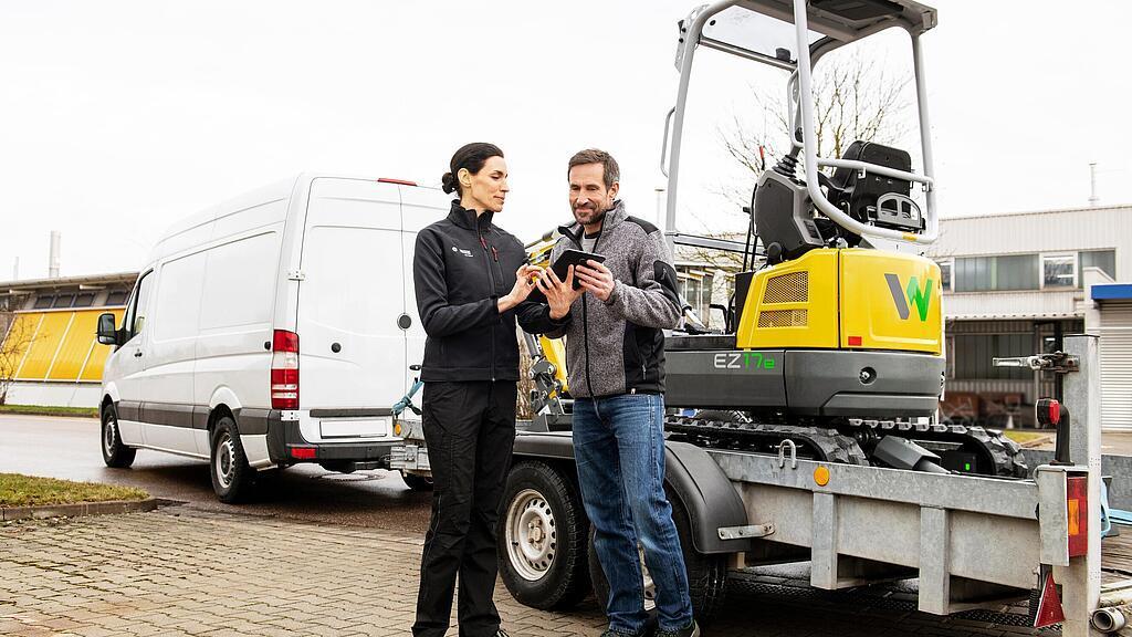 Wacker Neuson employee and customer in front of rented zero emission tracked excavator on a trailer.