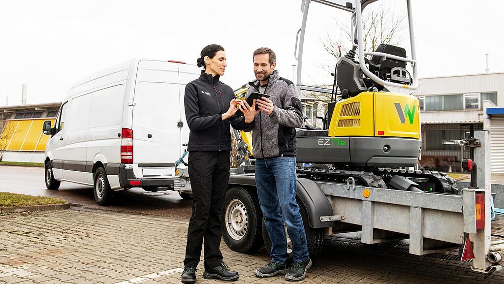 Wacker Neuson Mitarbeiterin und Kunde vor gemieteten zero emission Kettenbagger auf einem Anhänger.