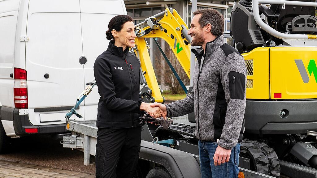 Wacker Neuson employee shaking a customer’s hand in front of a Wacker Neuson zero emission tracked excavator.