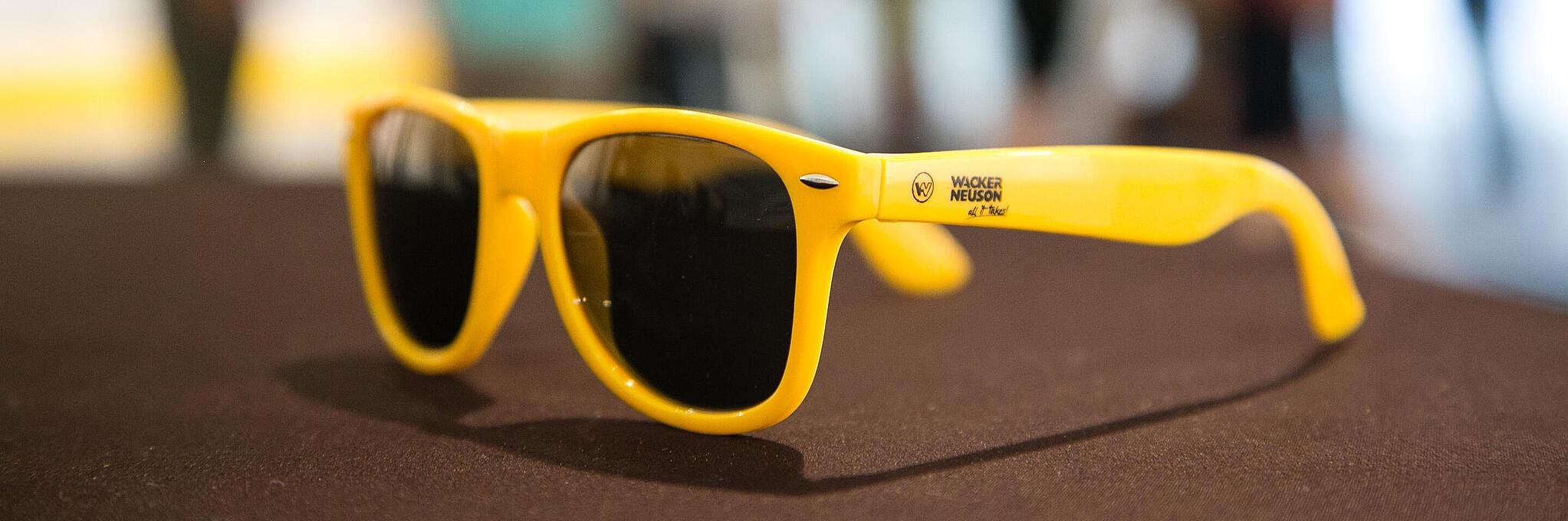 Gele zonnebril met Wacker Neuson-logo.