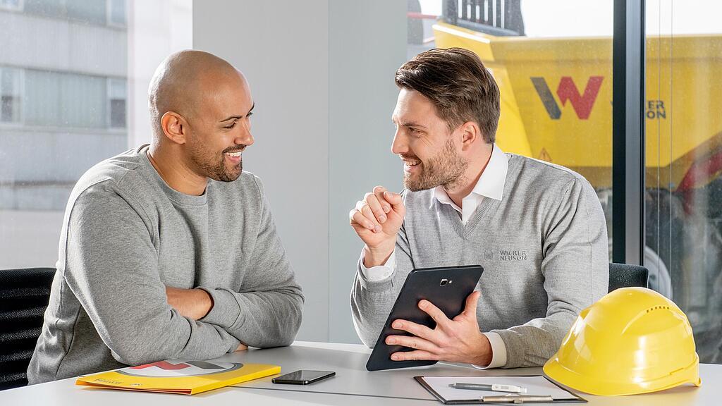 Wacker Neuson employee sitting at a desk and showing customer something on a tablet.