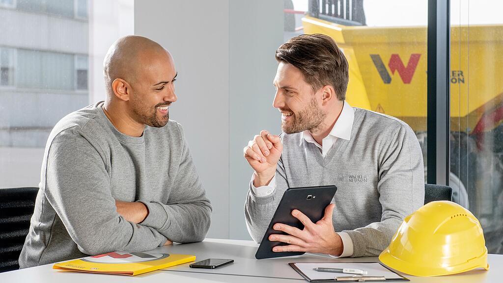 Wacker Neuson employee sitting at a desk and showing customer something on a tablet.