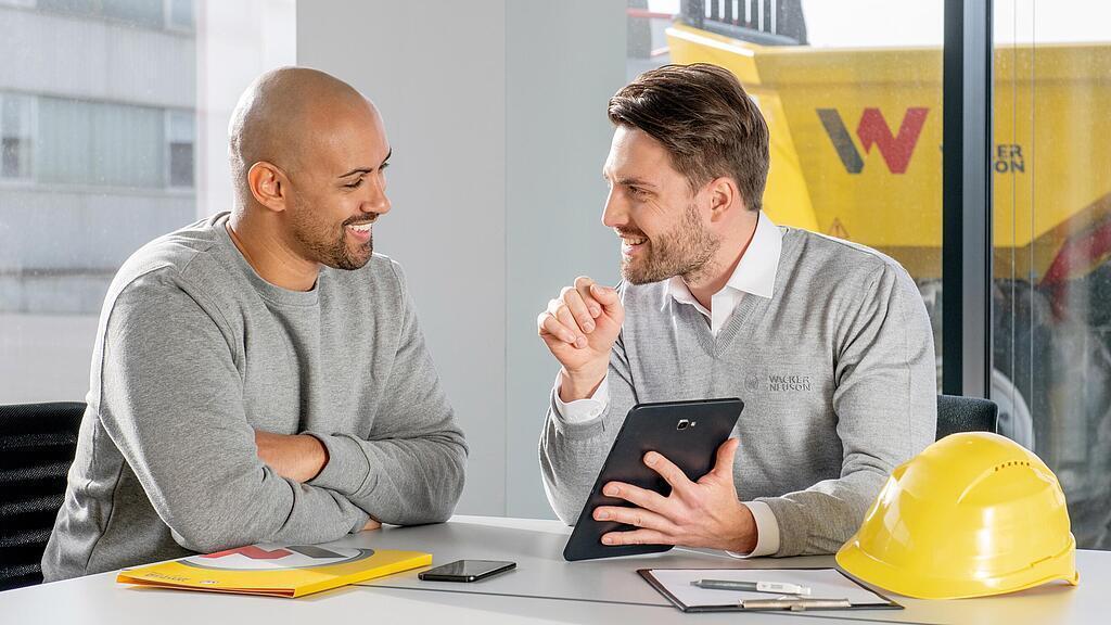 Wacker Neuson employee sitting at a desk and showing customer something on a tablet.