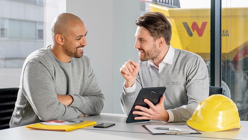 Wacker Neuson employee sitting at a desk and showing customer something on a tablet.