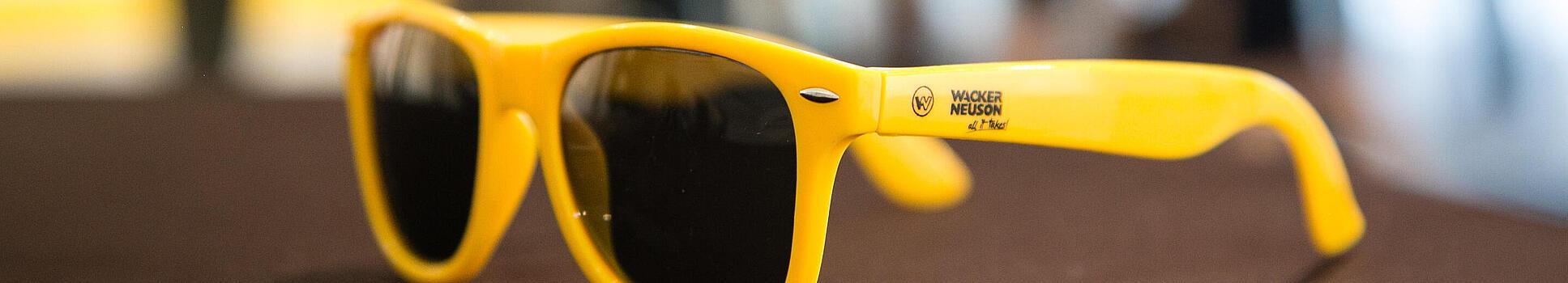 Gelbe Sonnenbrille mit Wacker Neuson Logo.