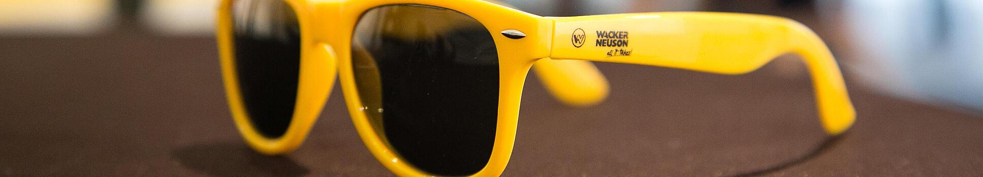 Yellow sunglasses with Wacker Neuson logo.