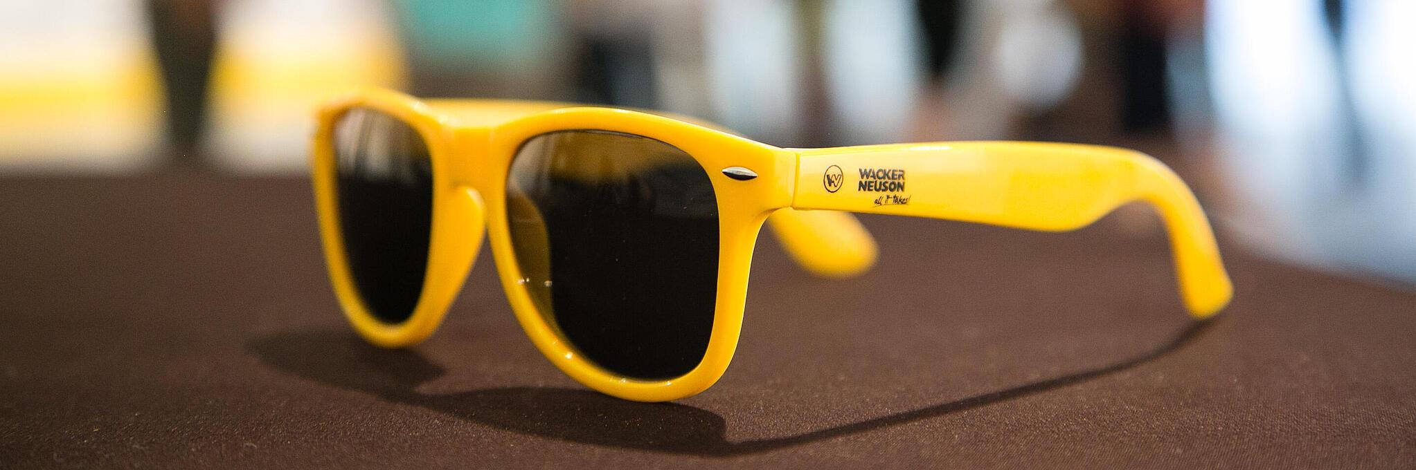 Yellow sunglasses with Wacker Neuson logo.