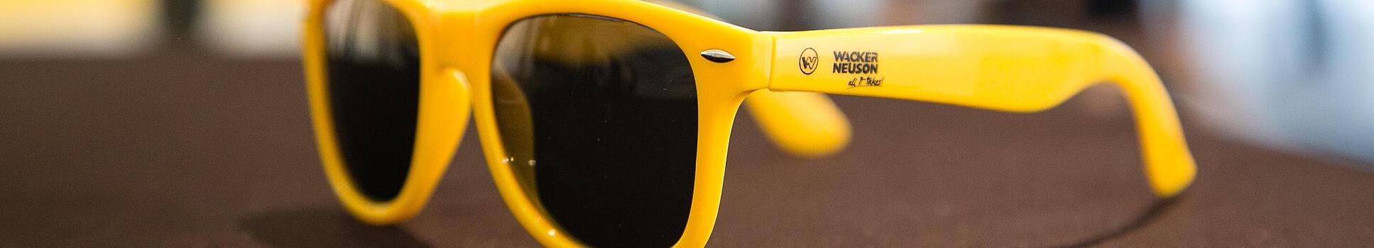 Yellow sunglasses with Wacker Neuson logo.