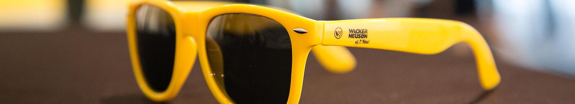 Gele zonnebril met Wacker Neuson-logo.