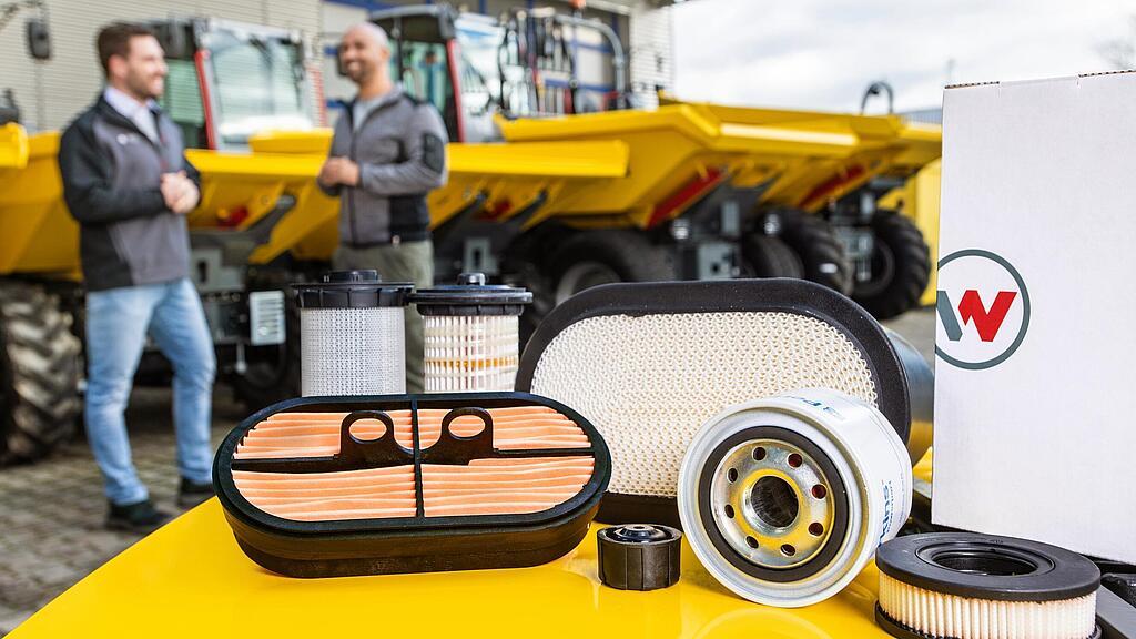 Wacker Neuson Ersatzteile auf Wacker Neuson Baumaschine, Wacker Neuson Berater, Kunde und Baumaschinen im Hintergrund.