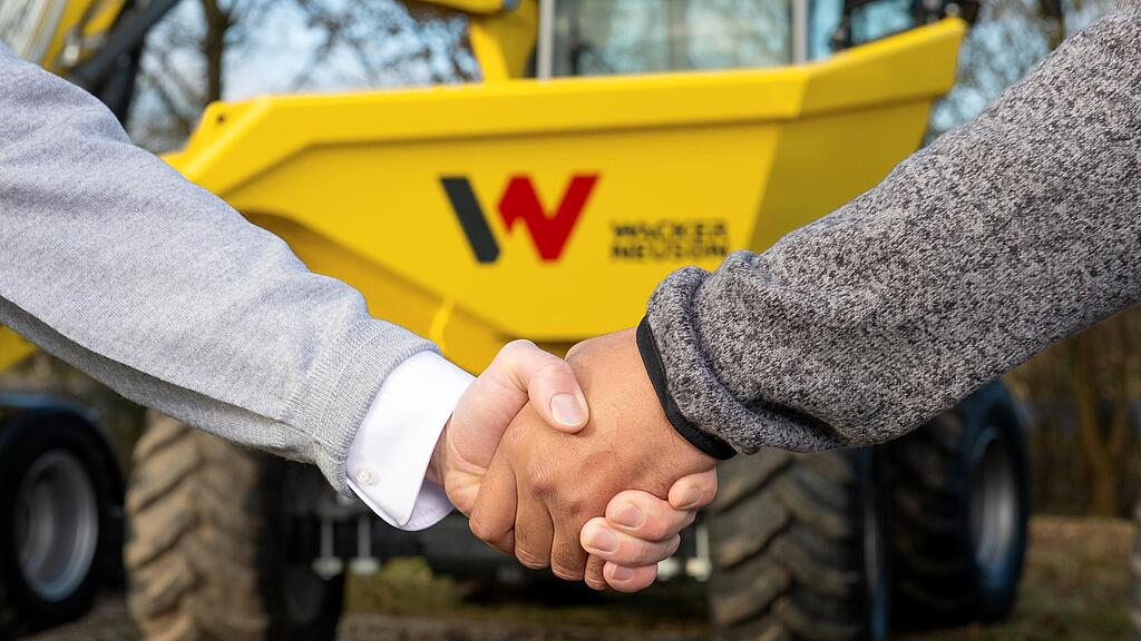 Poignée de mains entre une conseillère Wacker Neuson et un client devant un dumper Wacker Neuson.