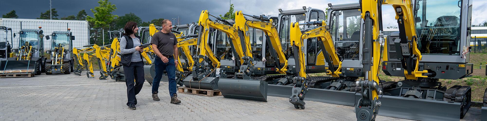 zwei personen laufen vor einer reihe von wacker neuson baggern