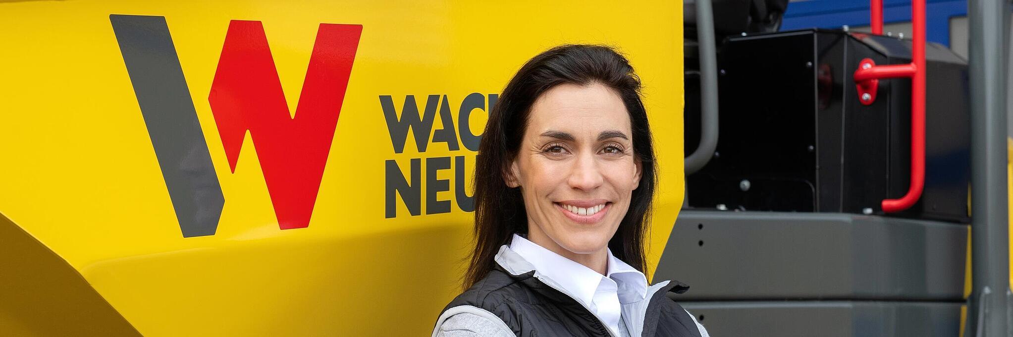 Een medewerker van Wacker Neuson staat glimlachend met gekruiste armen voor een Wacker Neuson-wieldumper.