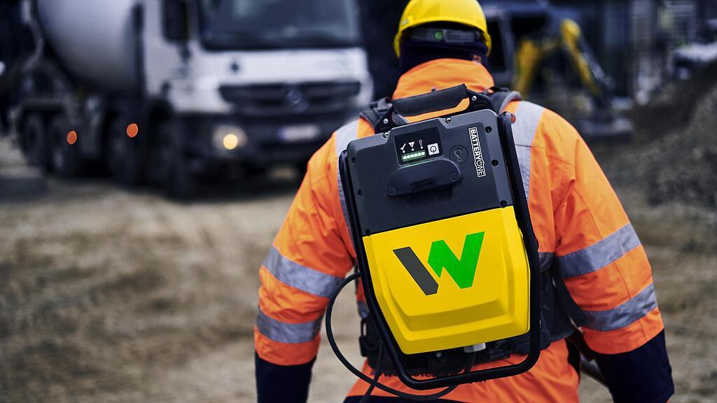 Trabalhador da construção carrega mochila com conversor de bateria recarregável da Wacker Neuson ACBe em um canteiro de obras.