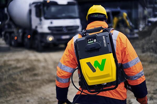 Un ouvrier porte le sac à dos pour convertisseur de batterie ACBe de Wacker Neuson sur un chantier.