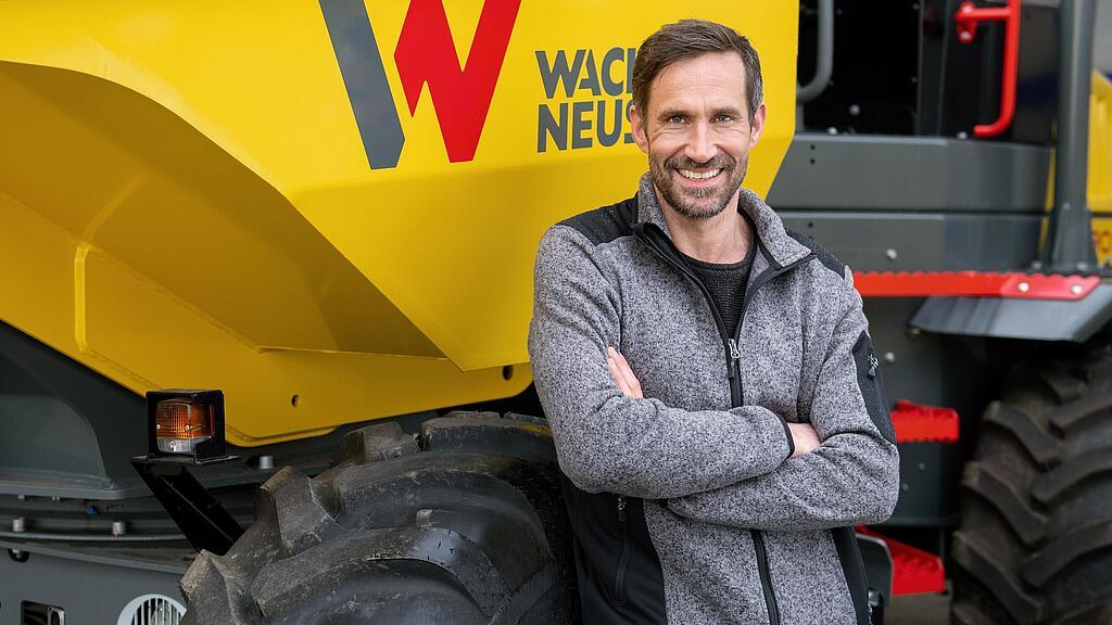 Uśmiechnięty klient firmy Wacker Neuson stoi ze skrzyżowanymi ramionami przed wozidłem kołowym Wacker Neuson.