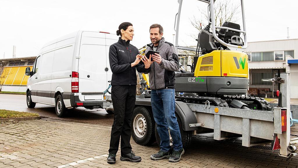 Pracowniczka firmy Wacker Neuson i klient podpisują umowę wynajmu przed koparką gąsienicową zero emission.