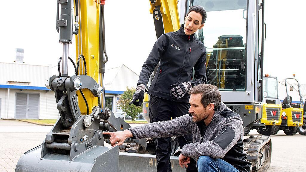 Wacker Neuson employee advising customer on attachment rental on a Wacker Neuson tracked excavator.