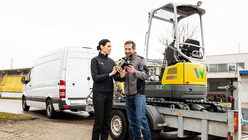 Wacker Neuson employee and customer in front of rented zero emission tracked excavator on a trailer.