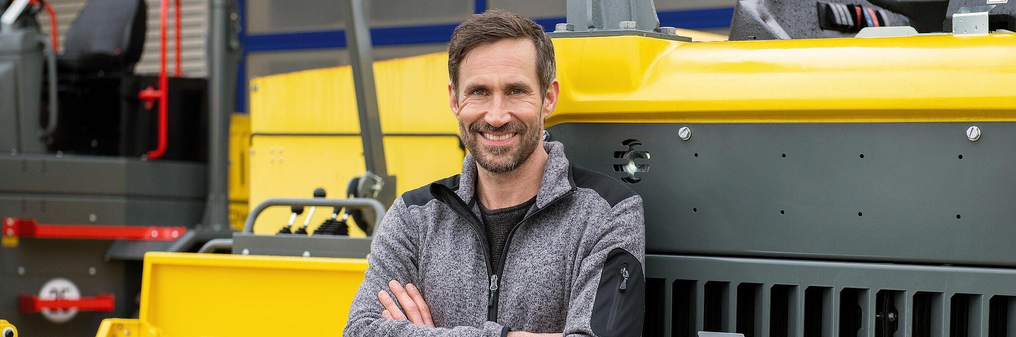 Smiling Wacker Neuson employee, arms crossed, leaning against a Wacker Neuson construction machine.