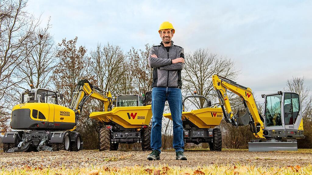 Een klant van Wacker Neuson staat glimlachend met gekruiste armen voor een Wacker Neuson-verhuurpark.