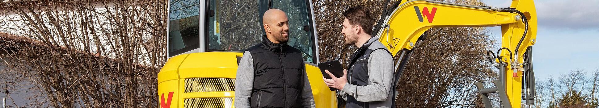 Wacker Neuson employee advising customer about the WeCare package in front of Wacker Neuson machines.