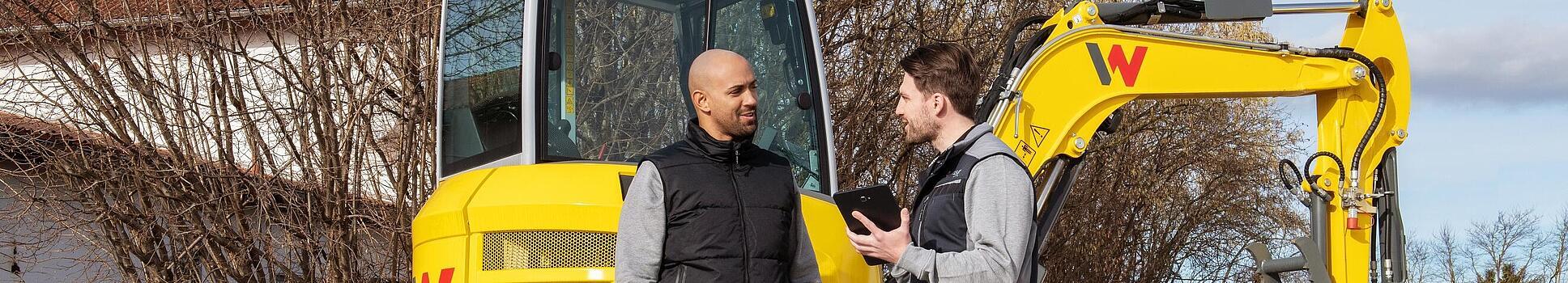 Wacker Neuson employee advising customer about the WeCare package in front of Wacker Neuson machines.