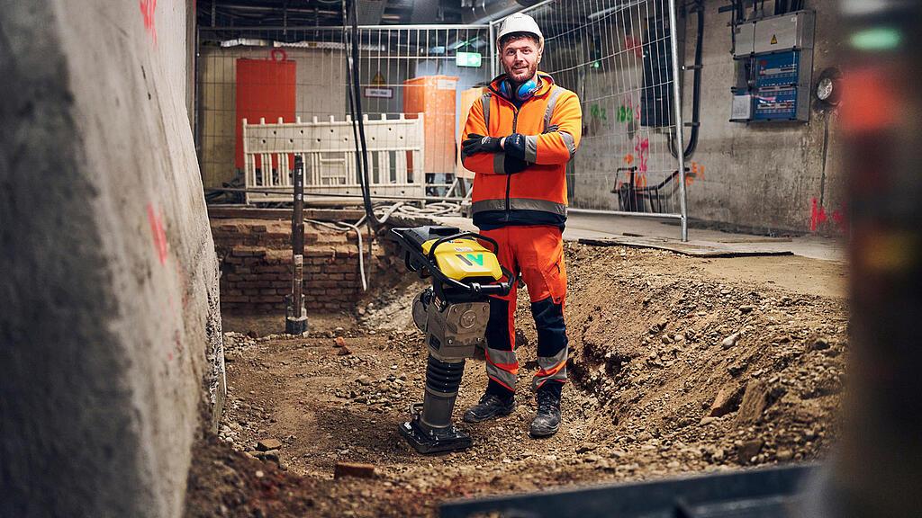 man standing next to battery powered rammer from wacker neuson at construction site