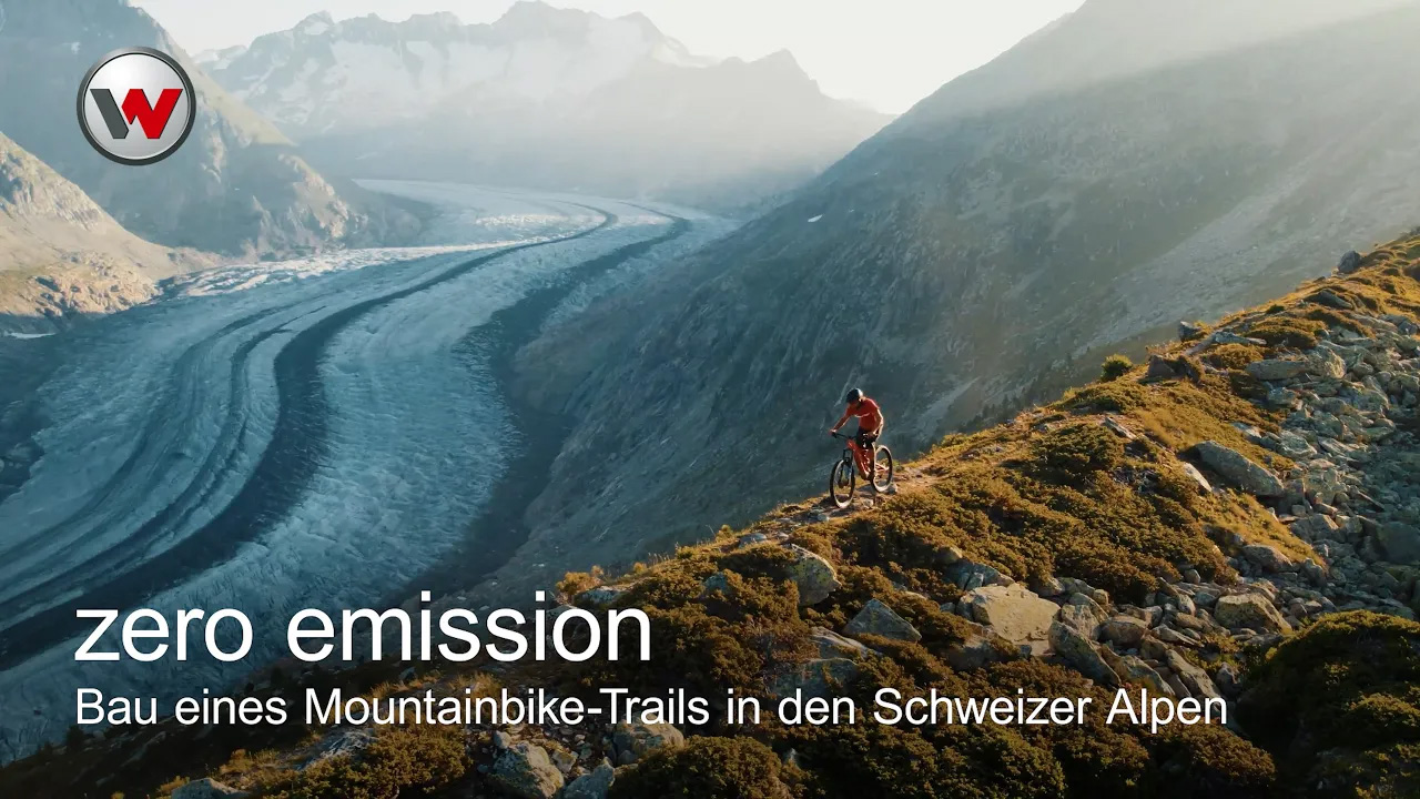 Ein Mann, der mit dem Mountainbike auf einem Bergrücken fährt, im Hintergrund schneebedeckte Berge