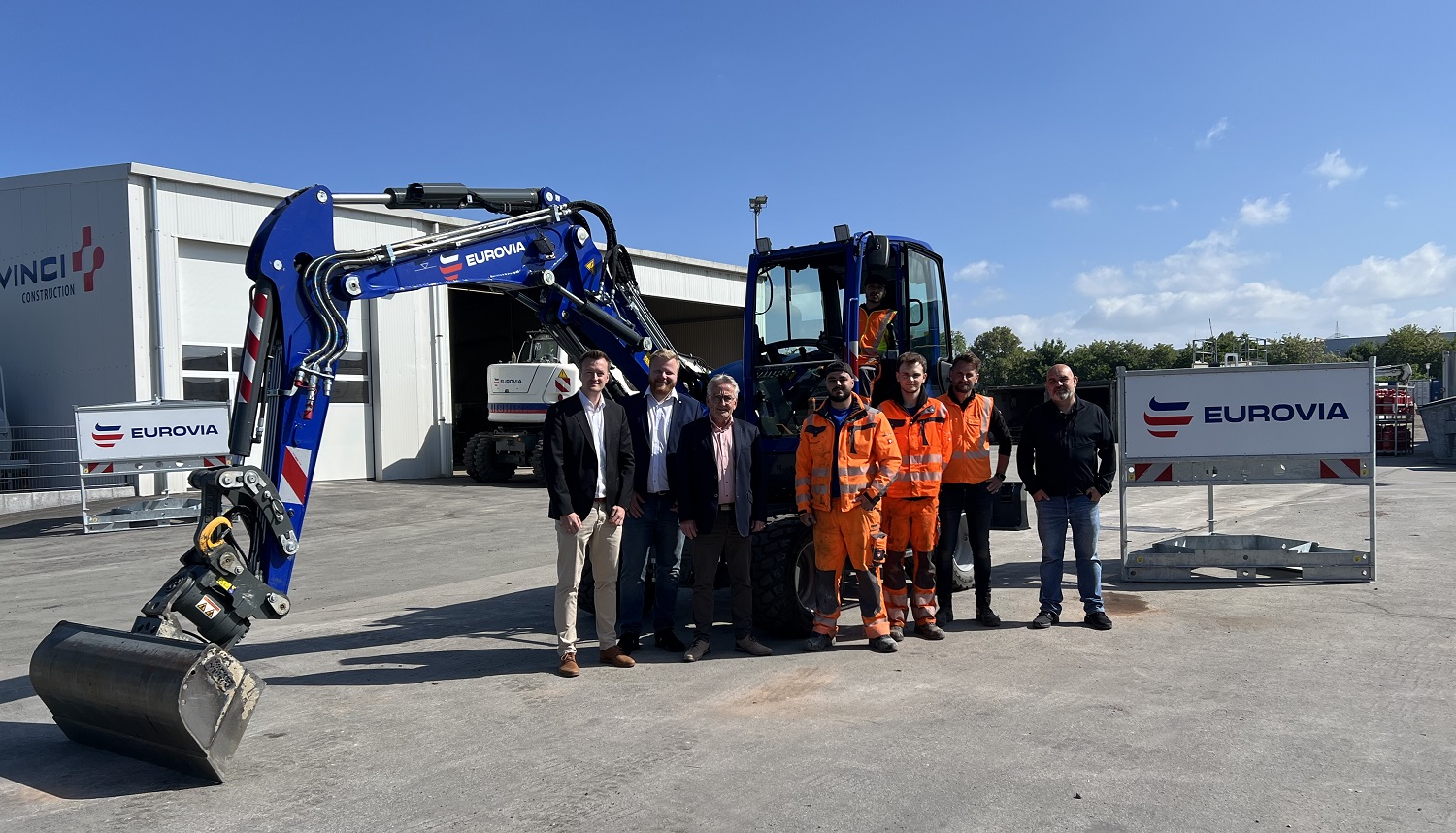 Bagger mit Auszubildenden im Vordergrund 